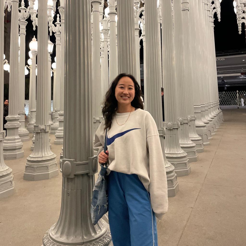 A photo of Mia smiling with an art installation of street lamps in the background.