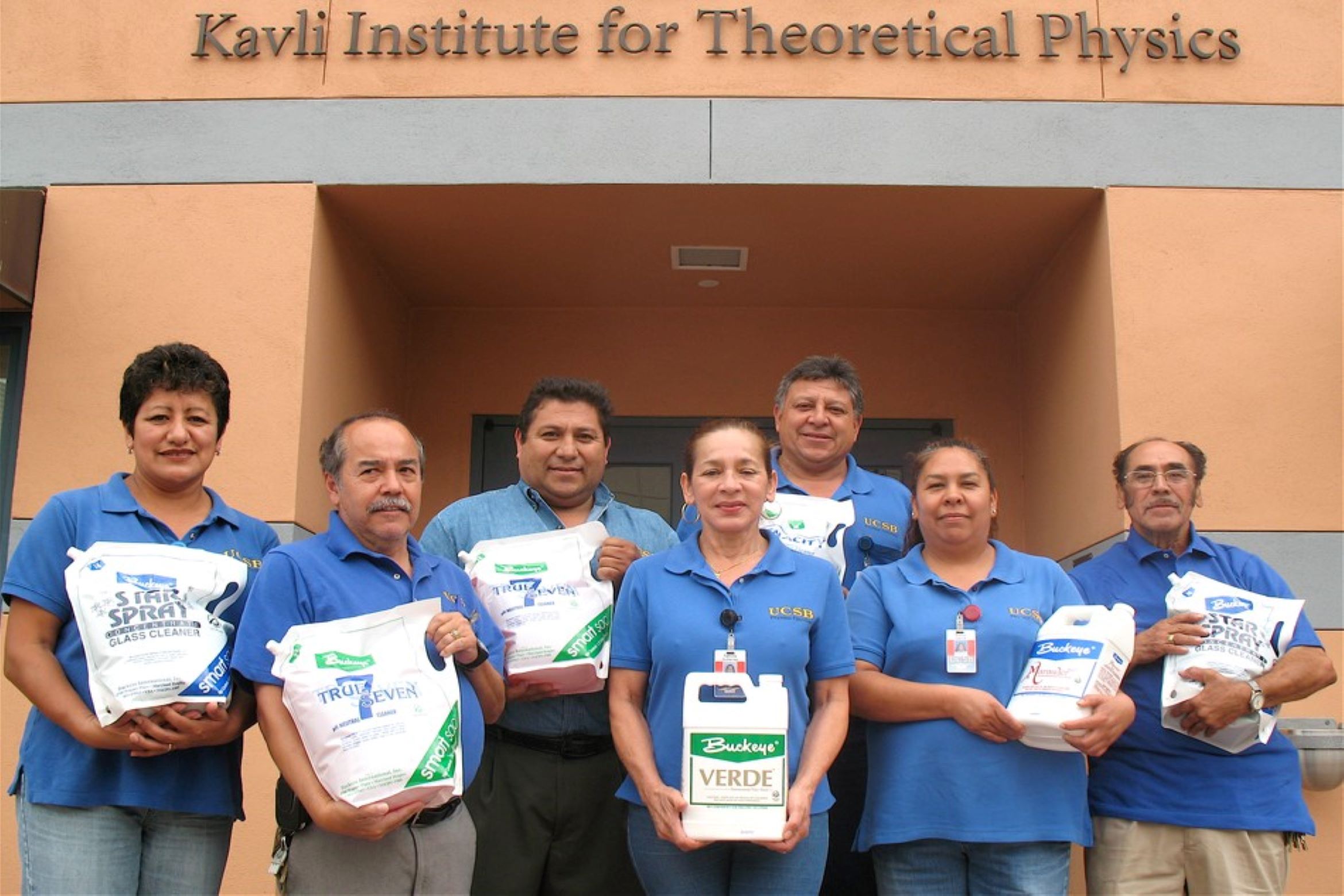 UC Santa Barbara staff holding green cleaning products standing in front of Kavli Institute for Theoretical Physics building sign