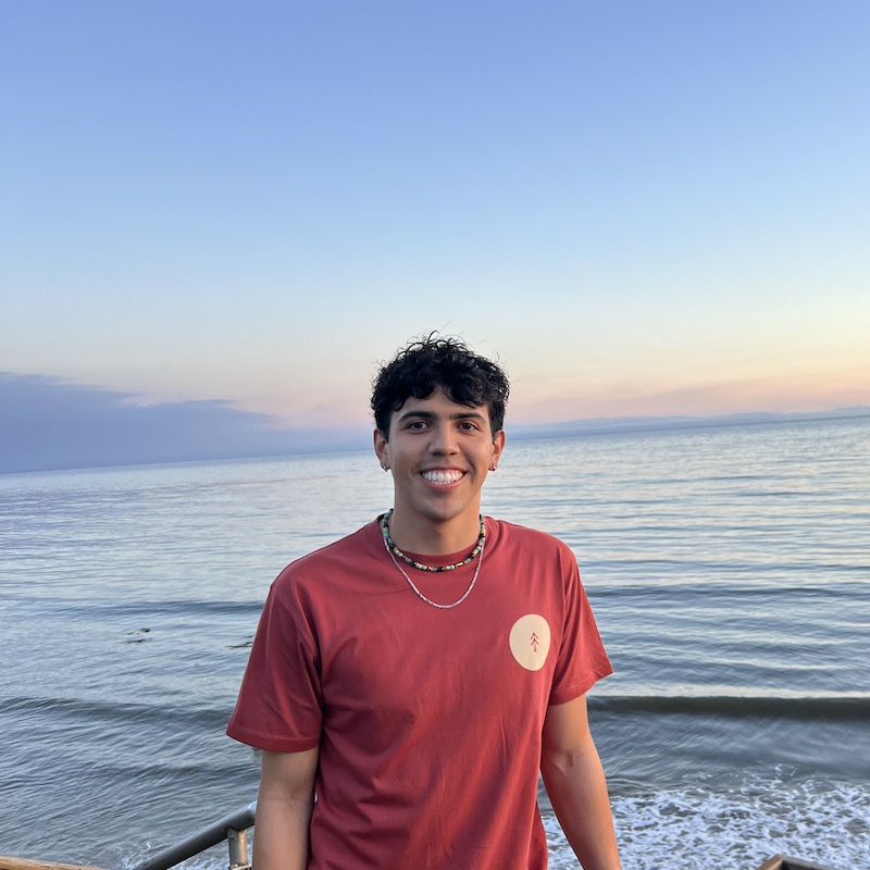 A photo of Anthony smiling with the ocean at sunset in the background.